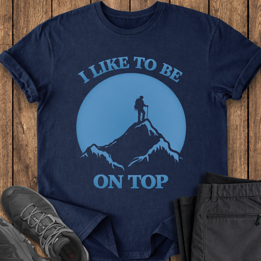 Navy blue t-shirt with mountain and hiker graphic and text 'I Like to Be on Top' on a wooden surface. funny hiking t shirt