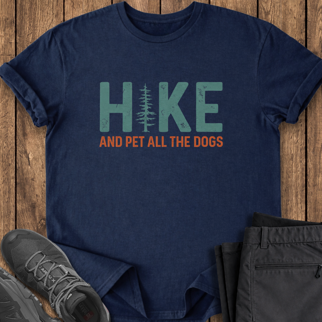 Navy blue t-shirt with 'Hike and Pet All the Dogs' text on a wooden surface with shoes and pants. dog lover hiking t shirt
