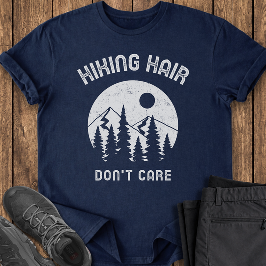 Navy blue t-shirt with 'Hiking Hair Don't Care' graphic on a wooden surface with hiking shoes and pants. funny hiking t shirt
