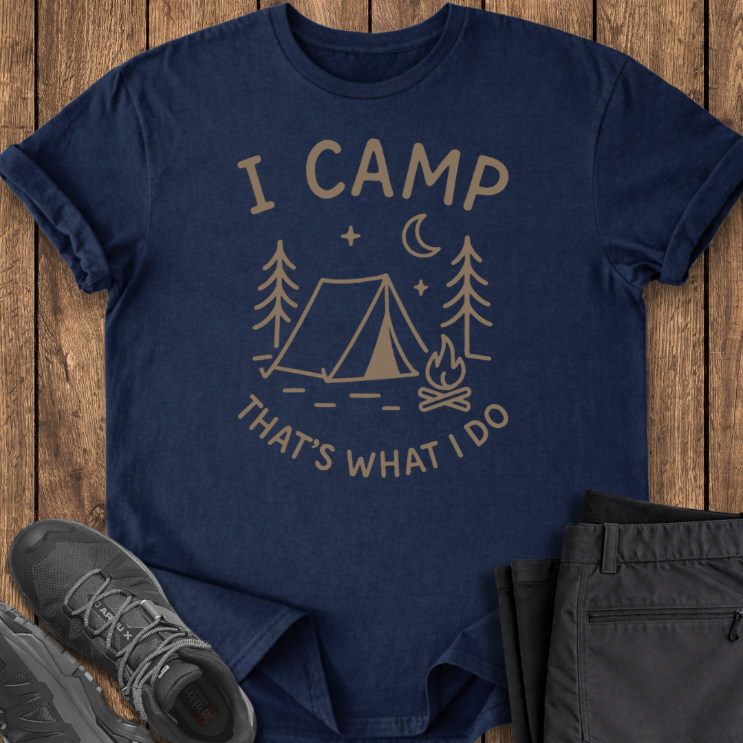 Navy blue t-shirt with 'I Camp, That's What I Do' design on a wooden surface with shoes and pants.
