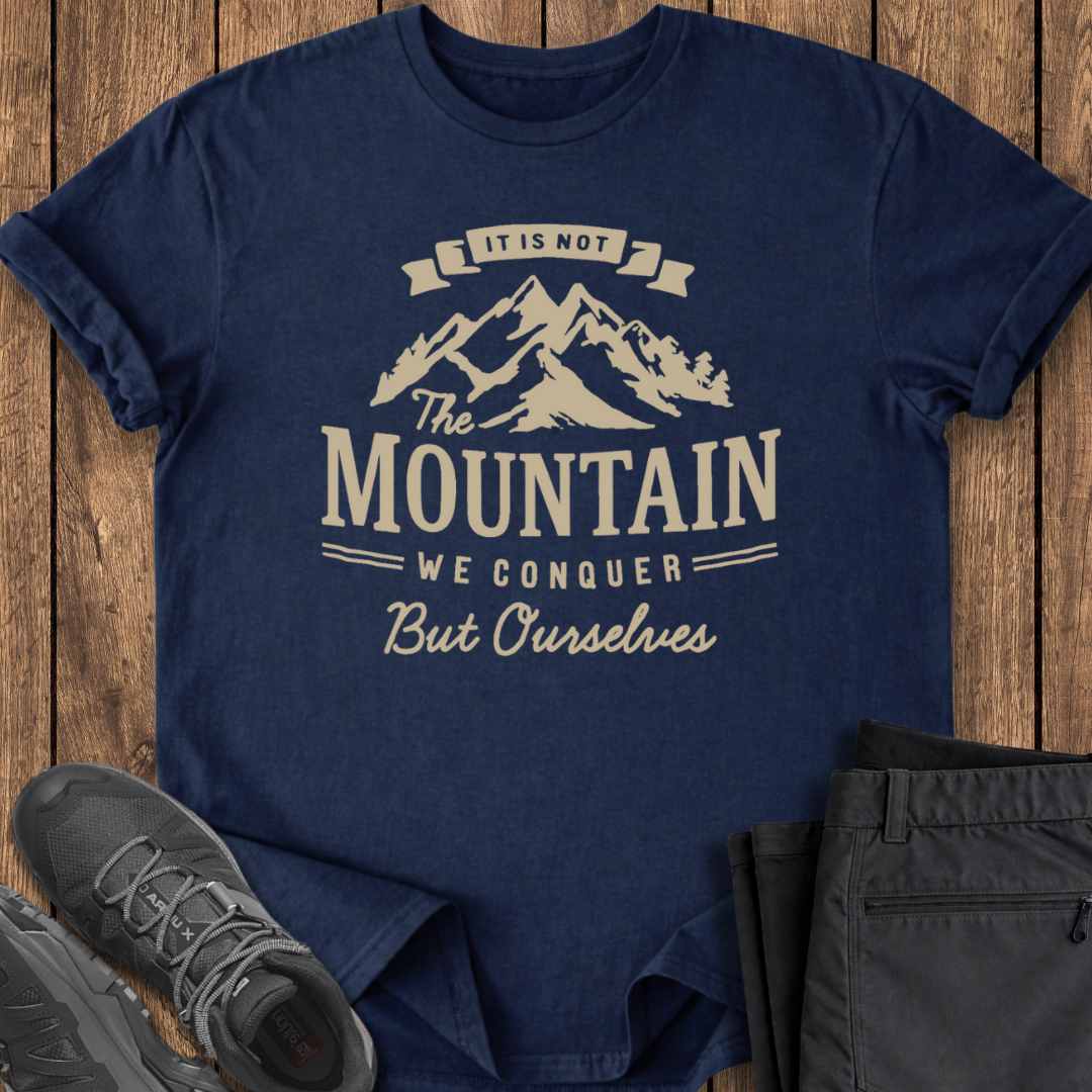 Navy blue t-shirt with mountain graphic and text on a wooden surface with shoes and pants.