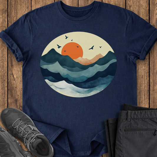 Navy blue t-shirt with a sunset and wave design on a wooden surface with shoes and pants.