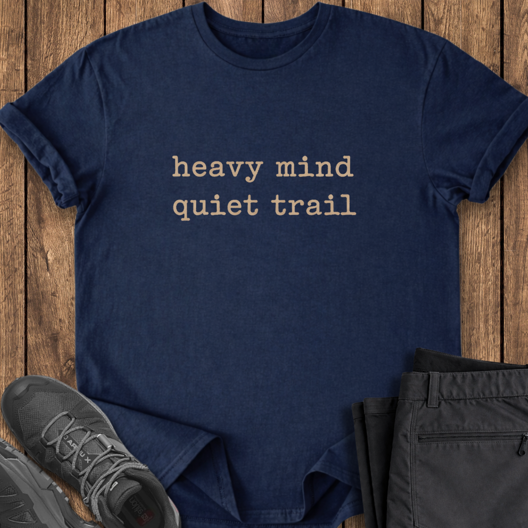 Navy blue t-shirt with 'heavy mind quiet trail' text on a wooden surface with shoes and pants. mental health outdoor shirt