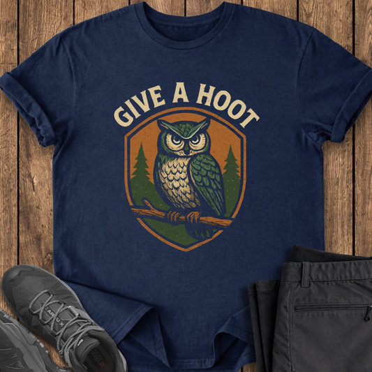 Navy blue t-shirt with owl graphic and 'Give a Hoot' text on a wooden surface, with shoes and pants for scale.