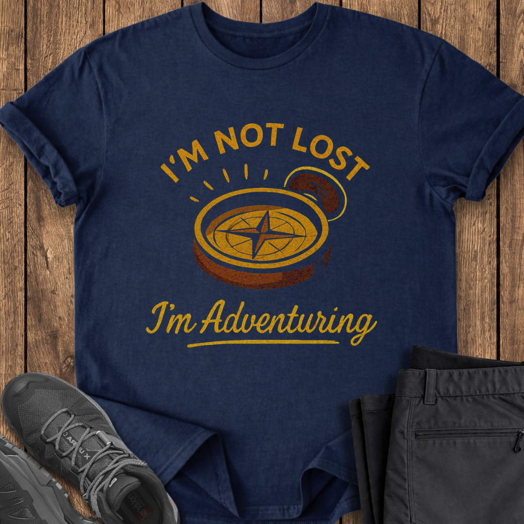 Navy blue t-shirt with 'I'm not lost, I'm adventuring' compass design on a wooden surface with shoes and pants. funny hiking t shirt