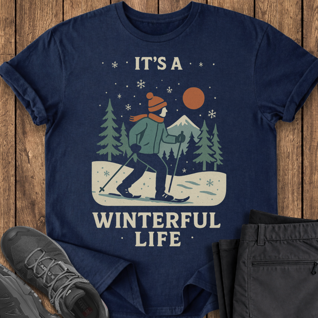 Navy blue t-shirt with winter-themed graphic and text 'It's a Winterful Life' on a wooden surface.