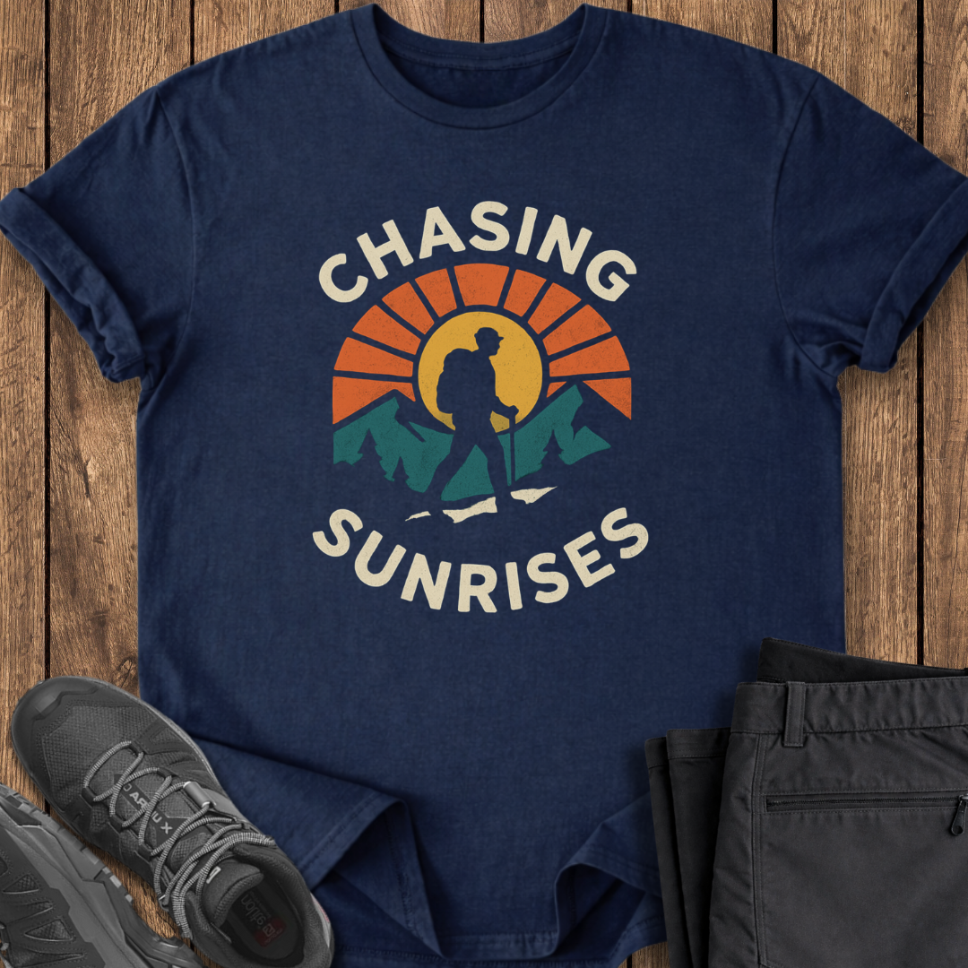 Navy blue t-shirt with 'Chasing Sunrises' graphic on a wooden surface with shoes and pants.