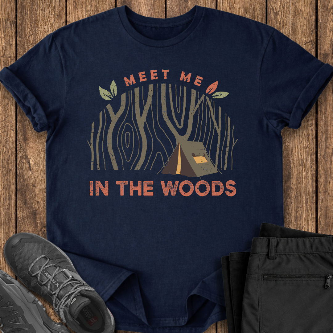 Navy blue t-shirt with 'Meet Me in the Woods' graphic on a wooden surface with shoes and pants.