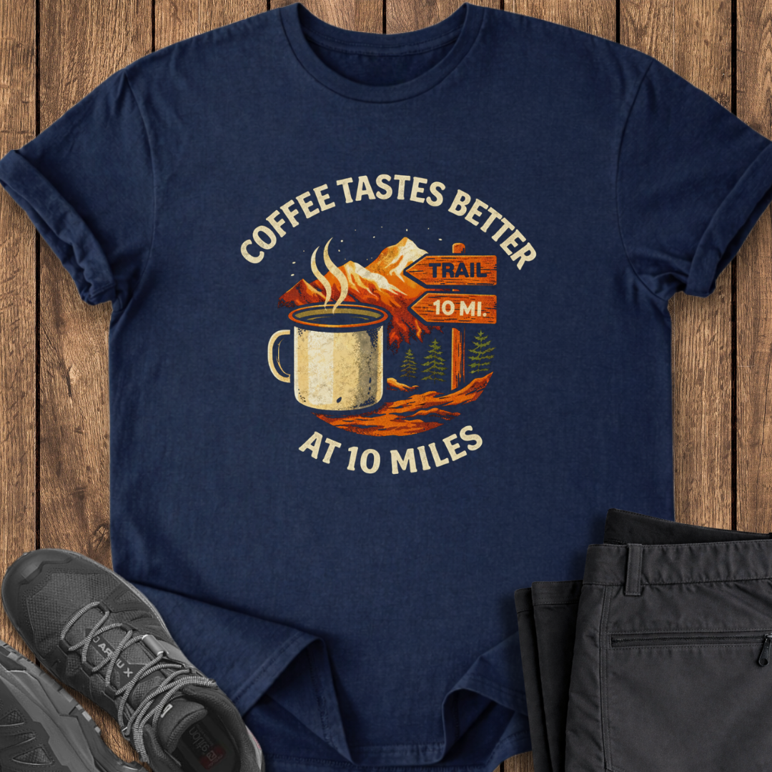 Navy blue t-shirt with coffee-themed graphic on a wooden surface with shoes and pants. coffee hiking t shirt
