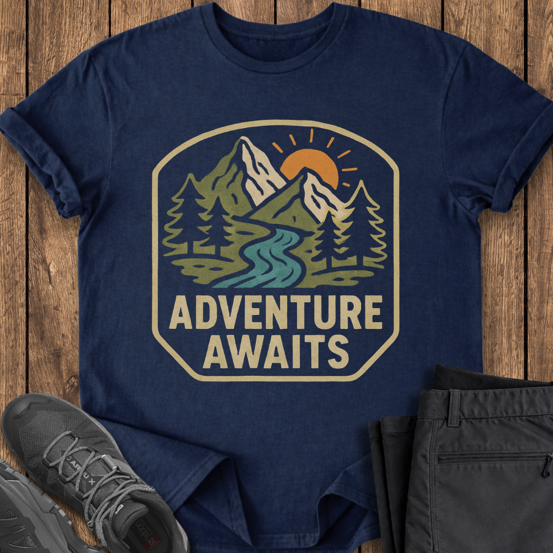 Navy blue t-shirt with 'Adventure Awaits' graphic on a wooden surface with shoes and pants. adventure outdoor t shirt