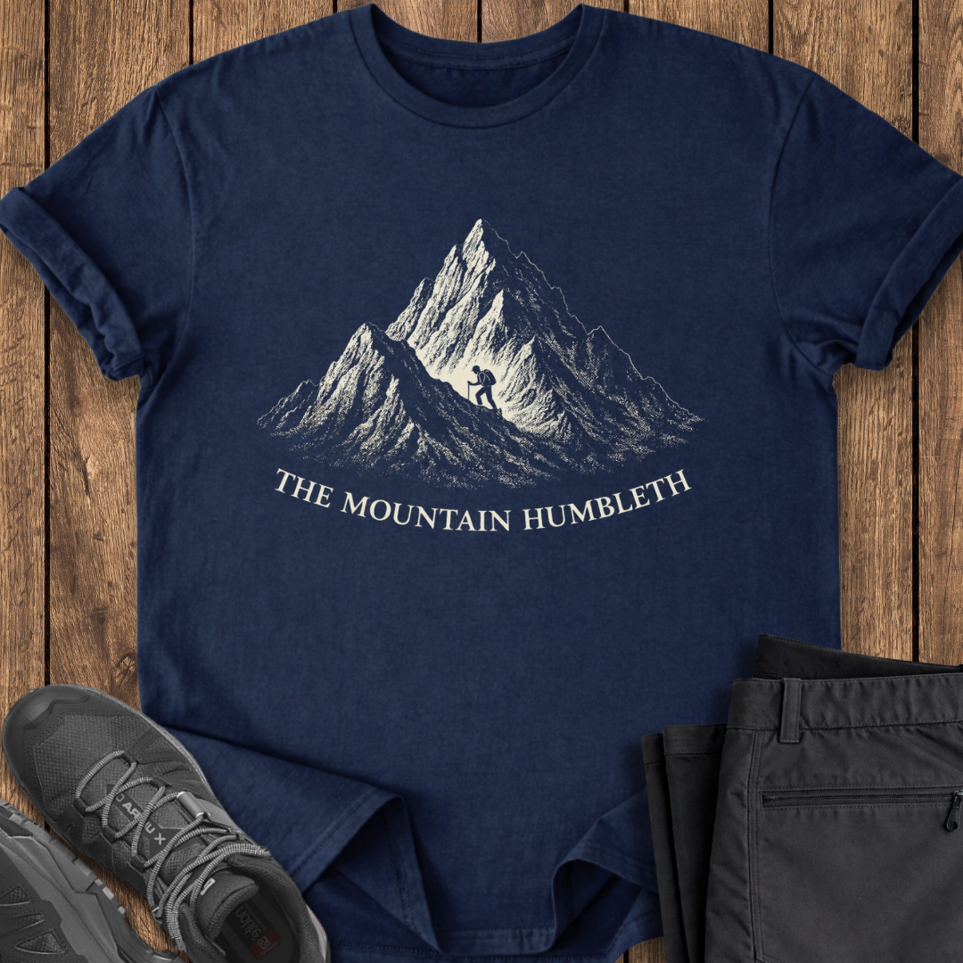 Navy blue t-shirt with mountain graphic and text on a wooden surface, accompanied by gray shoes and black pants. funny mountain adventure t shirt