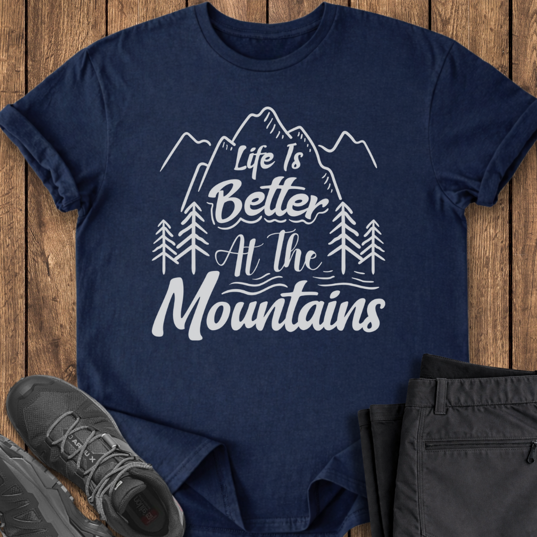Navy blue t-shirt with 'Life is Better at the Mountains' text on a wooden surface with shoes and pants.