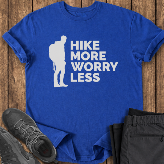Blue t-shirt with 'Hike More Worry Less' design on a wooden surface with hiking shoes and pants.