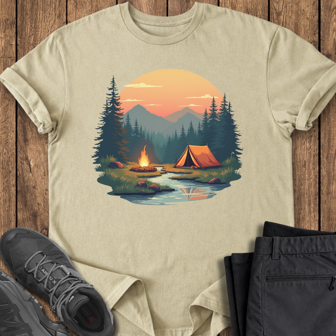 Beige t-shirt with a camping scene design on a wooden surface with shoes and pants.