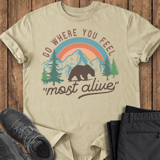 Beige t-shirt with bear graphic and text on a wooden surface with shoes and pants.
