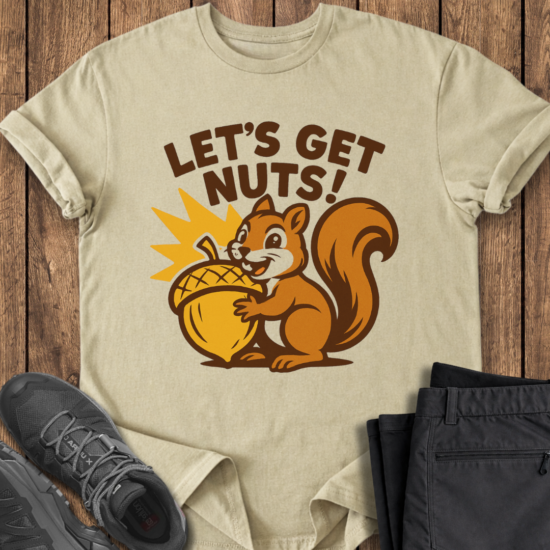 Beige t-shirt with a cartoon squirrel and 'Let's Get Nuts!' text on a wooden surface with shoes and pants.