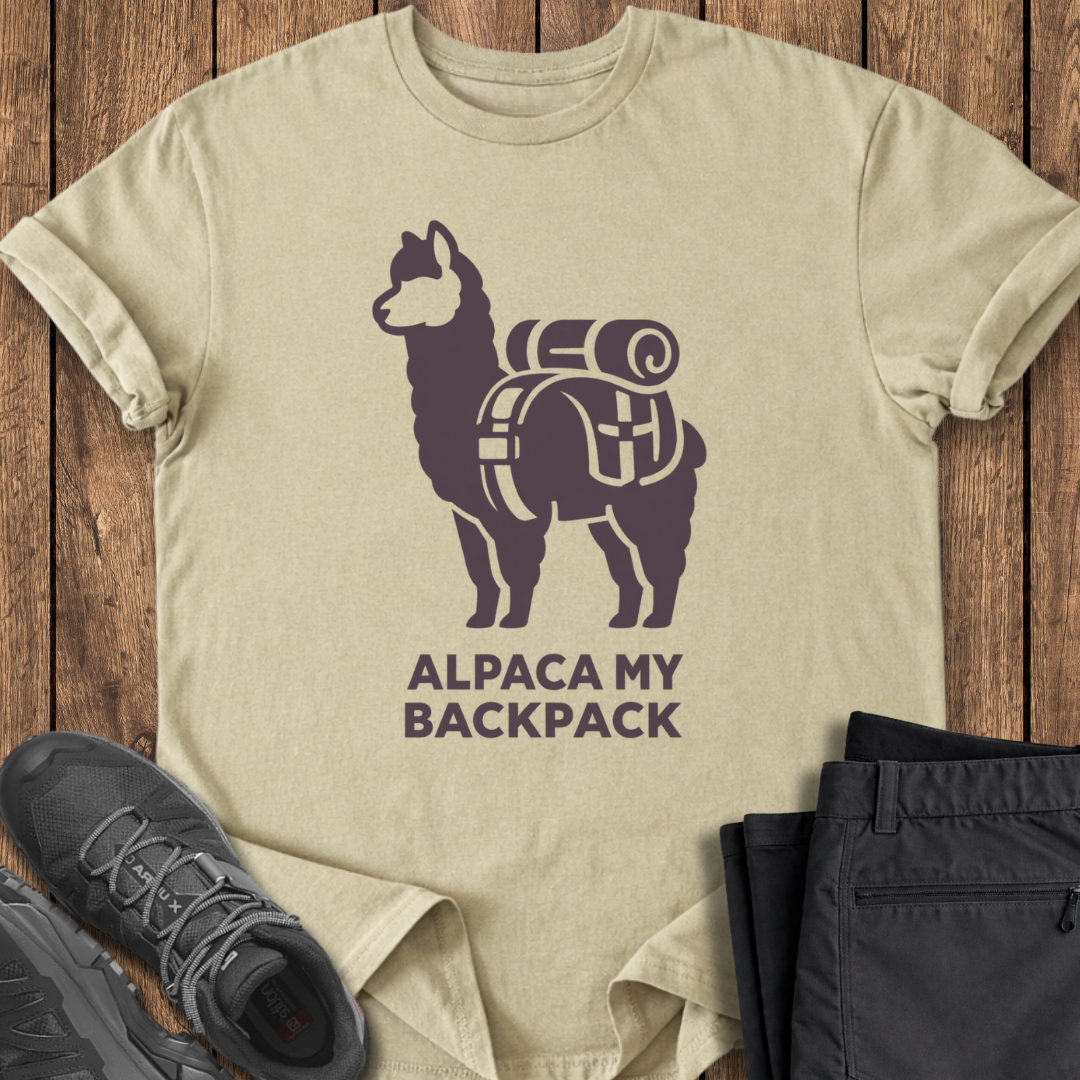 Beige t-shirt with alpaca graphic and 'Alpaca My Backpack' text on a wooden surface, with shoes and pants for scale. funny backpacking shirt