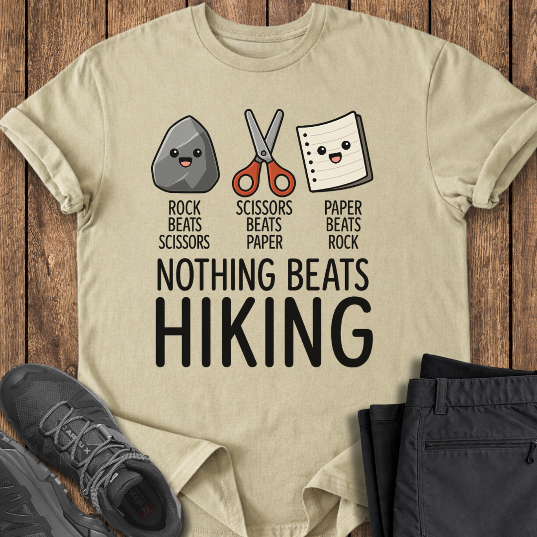 Beige t-shirt with rock, scissors, paper graphic and 'Nothing Beats Hiking' text on a wooden surface with hiking shoes and pants.