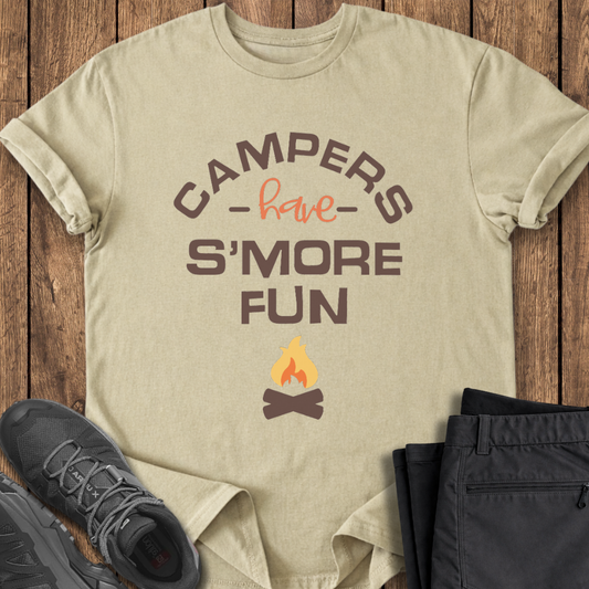 Beige t-shirt with 'Campers have S'more Fun' text and campfire graphic on a wooden surface with shoes and pants. funny campfire t shirt