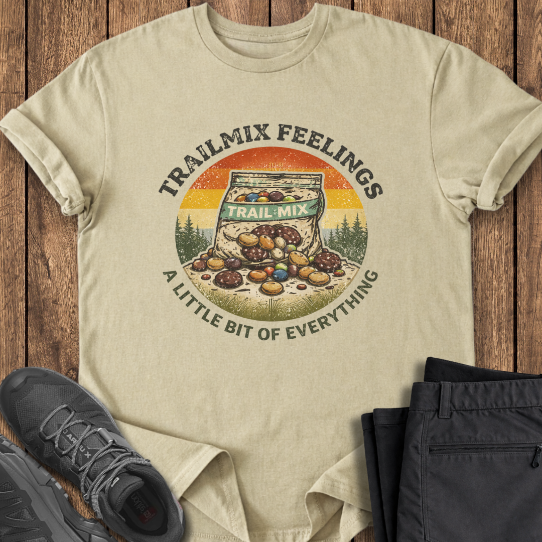 Beige t-shirt with 'Trailmix Feelings' graphic on a wooden surface with shoes and pants. funny hiking t shirt