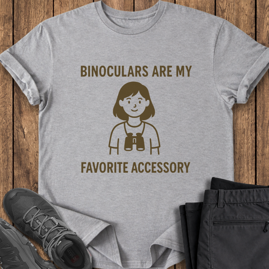 Gray t-shirt with binoculars graphic and text on a wooden surface with shoes and pants.
