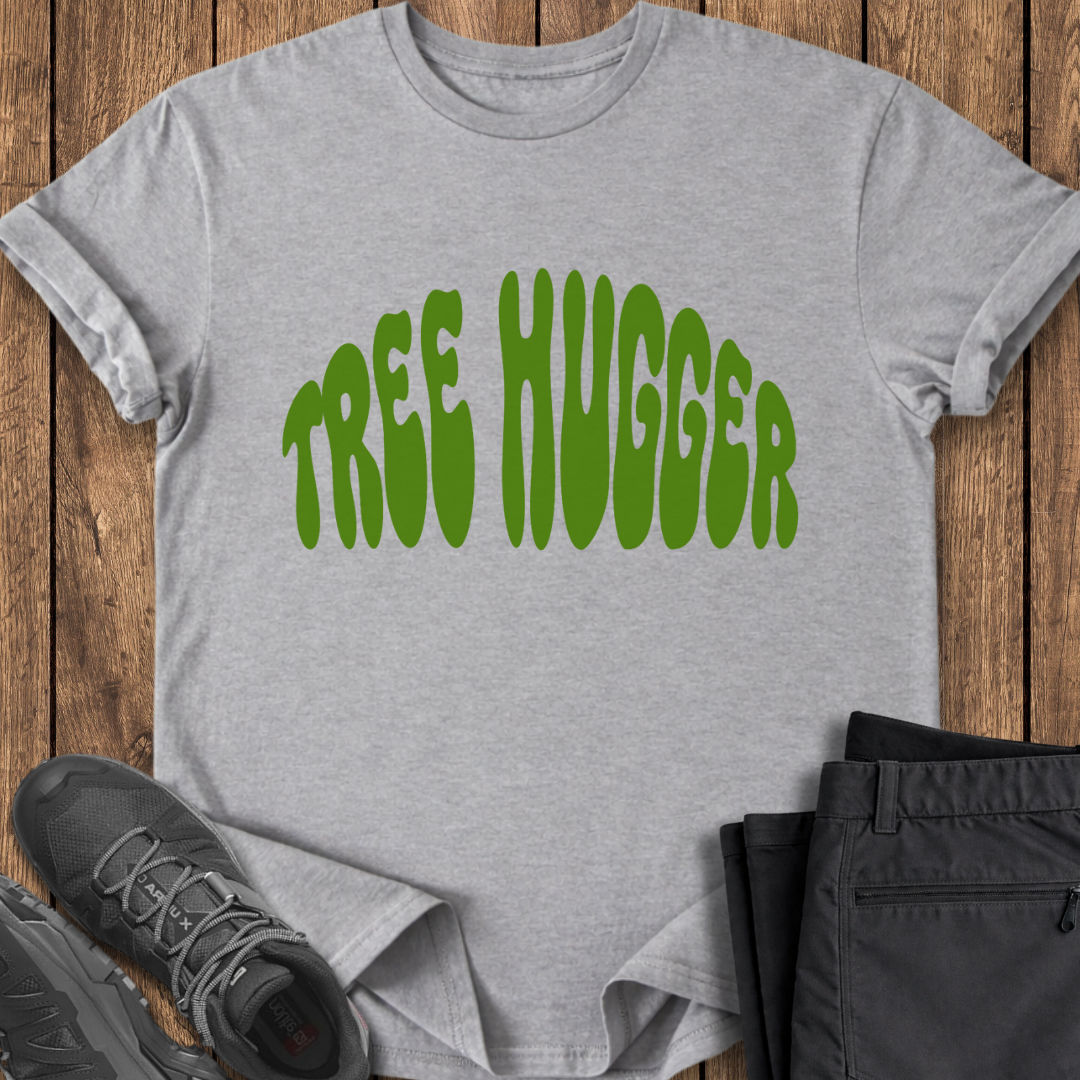 Gray t-shirt with 'TREE HUGGER' text in green on a wooden surface with shoes and pants.