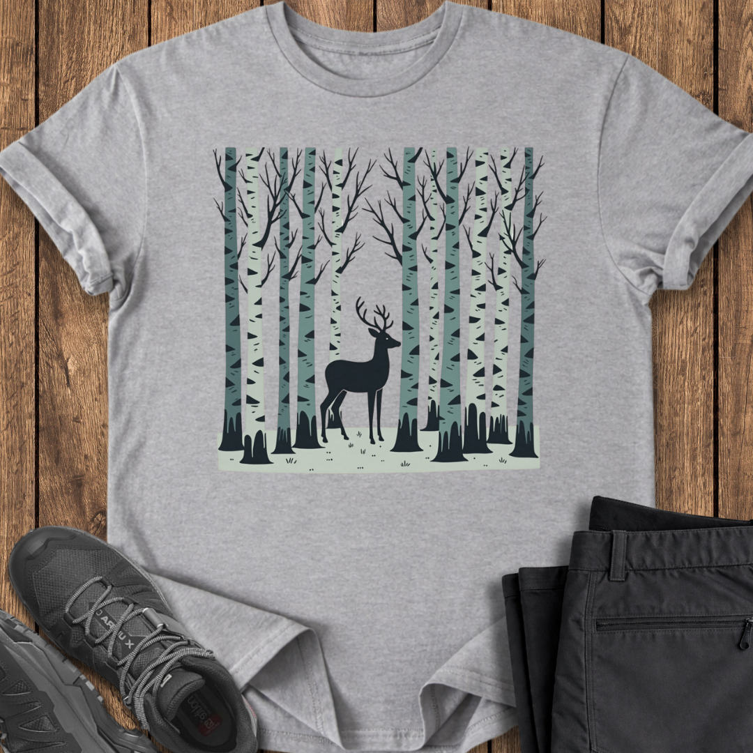 Gray t-shirt with a deer in a forest design on a wooden surface with shoes and pants.