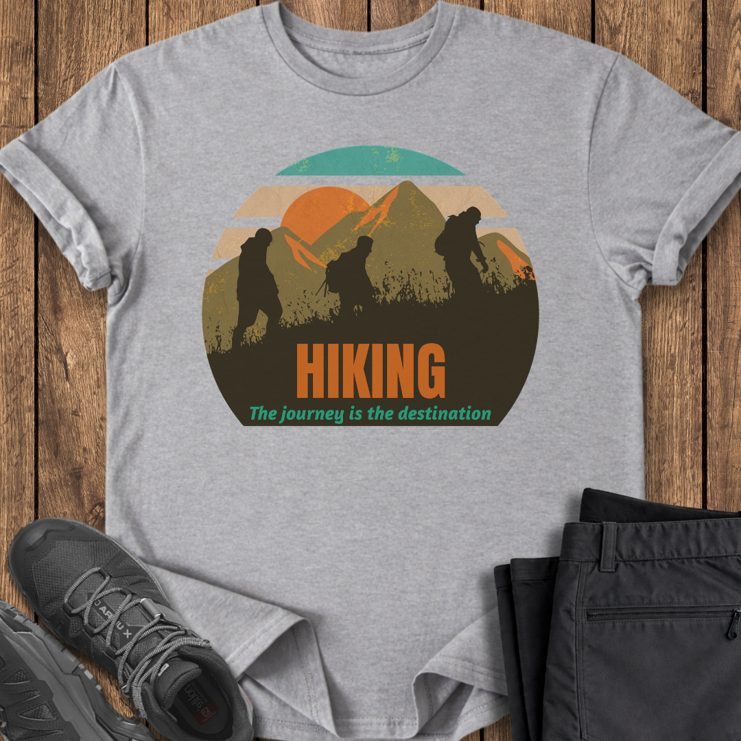 Gray t-shirt with hiking graphic and text on a wooden surface with shoes and pants. three backpacker mountains mountaineers mindful t shirt