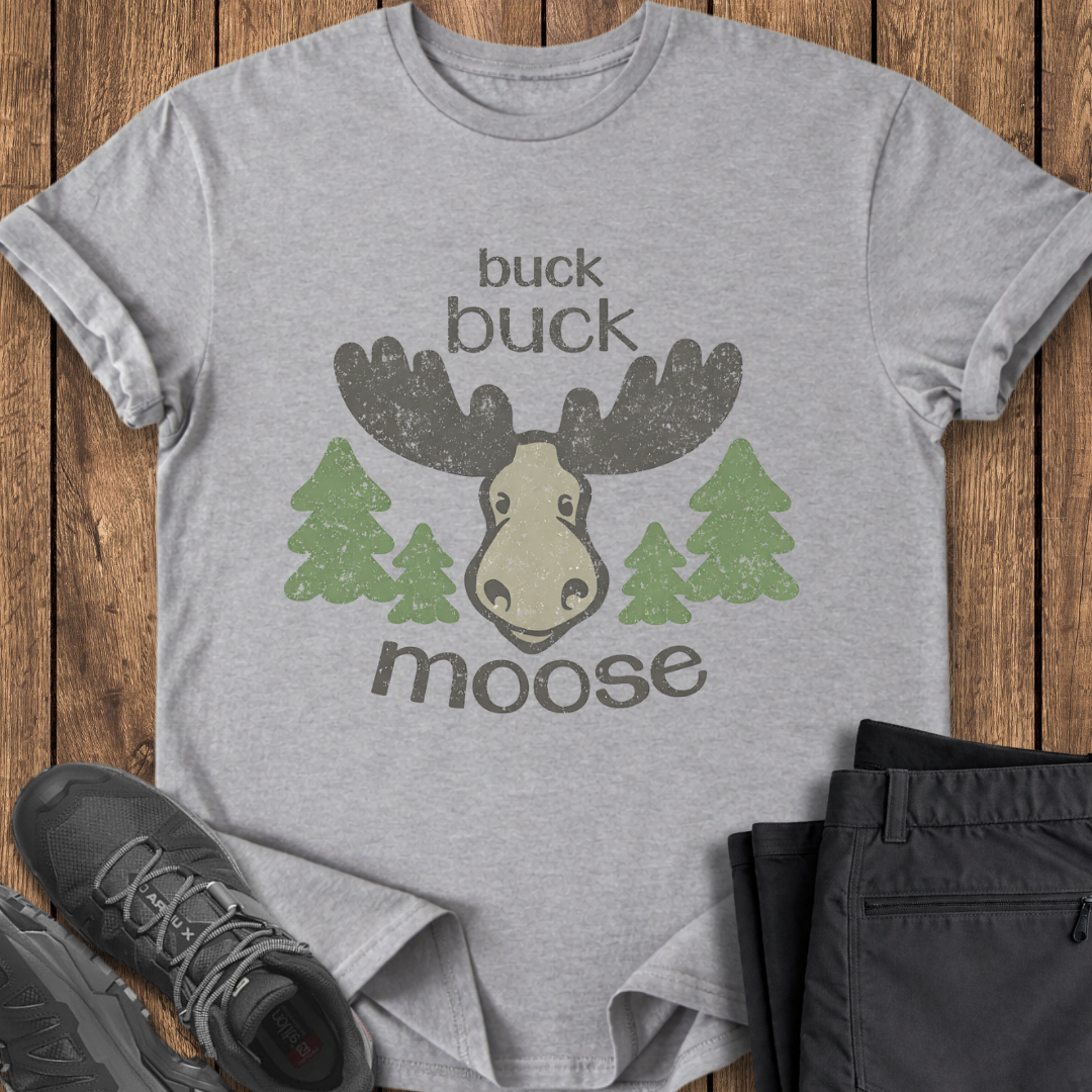 Gray t-shirt with moose graphic and text on a wooden surface with shoes and pants. funny moose t shirt