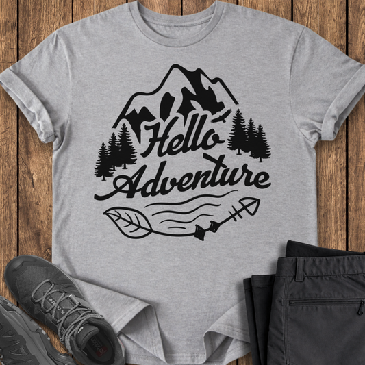 Gray t-shirt with 'Hello Adventure' design on a wooden surface with shoes and pants. adventure t shirt