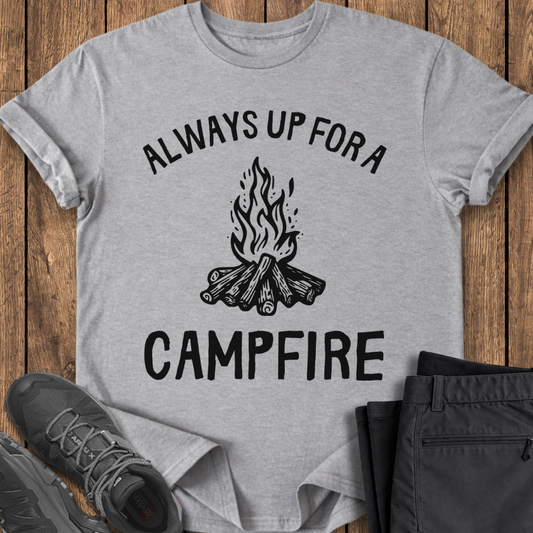 Gray t-shirt with 'Always Up For a Campfire' design on a wooden surface with shoes and pants. camp camping t shirt