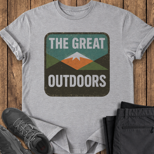 Gray t-shirt with 'The Great Outdoors' graphic on a wooden surface with shoes and pants. mountain outdoor t shirt