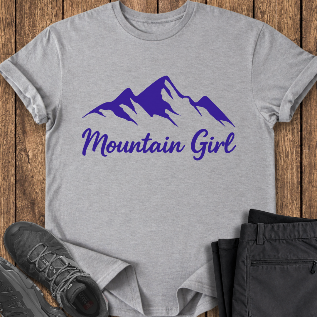 Gray t-shirt with purple mountain design and 'Mountain Girl' text on a wooden surface with shoes and pants.