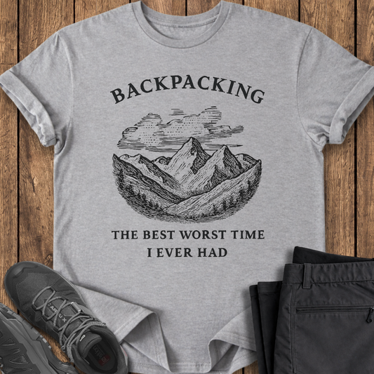 Gray t-shirt with mountain graphic and text on a wooden surface with shoes and pants. funny backpacking shirt