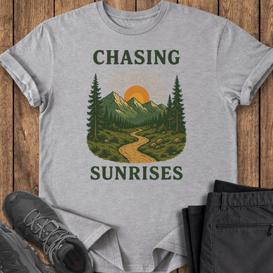 Gray t-shirt with nature graphic and 'Chasing Sunrises' text on a wooden surface with shoes and pants.