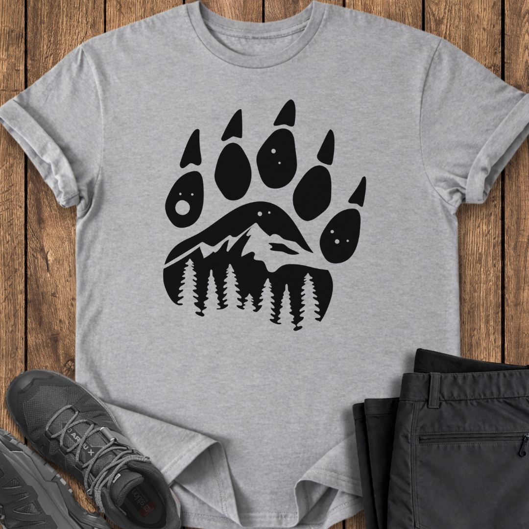Gray t-shirt with black bear paw print design on a wooden surface with shoes and pants. bear forest mountain pine outdoor t shirt