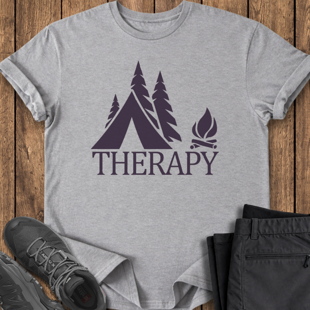 Gray t-shirt with purple camping graphic and 'THERAPY' text on a wooden surface with shoes and pants.