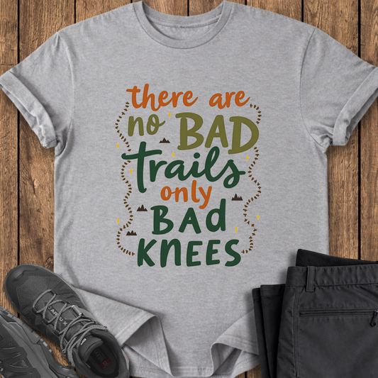 Gray t-shirt with hiking-themed text on a wooden surface with shoes and pants.