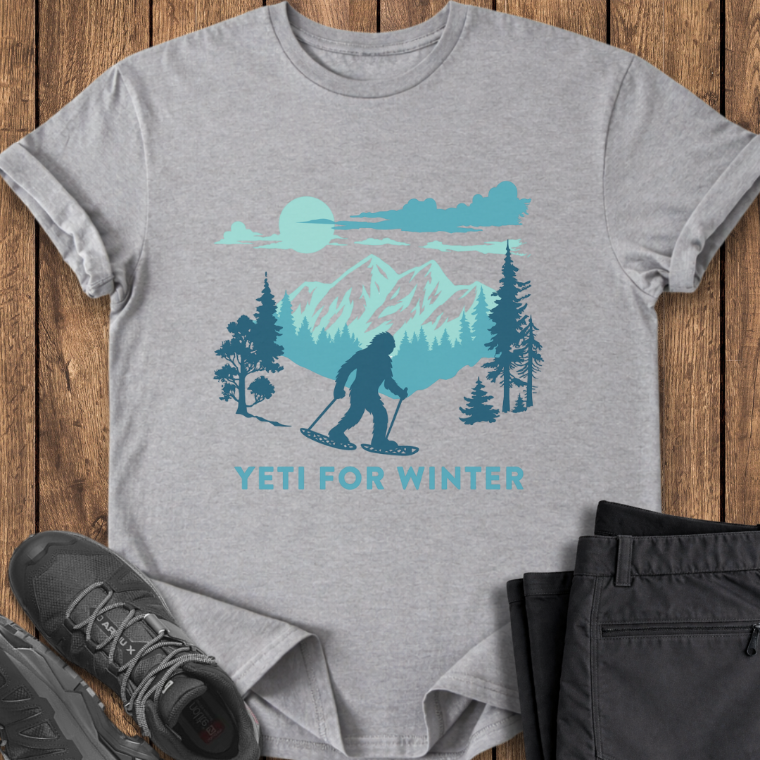 Gray t-shirt with a Yeti for Winter graphic on a wooden surface with shoes and pants.