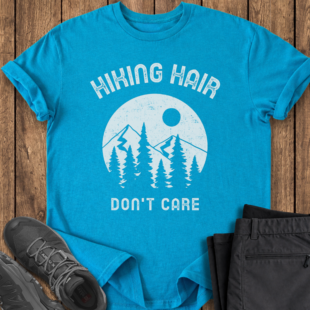 Blue t-shirt with 'Hiking Hair Don't Care' graphic on a wooden surface with shoes and pants. funny hiking t shirt