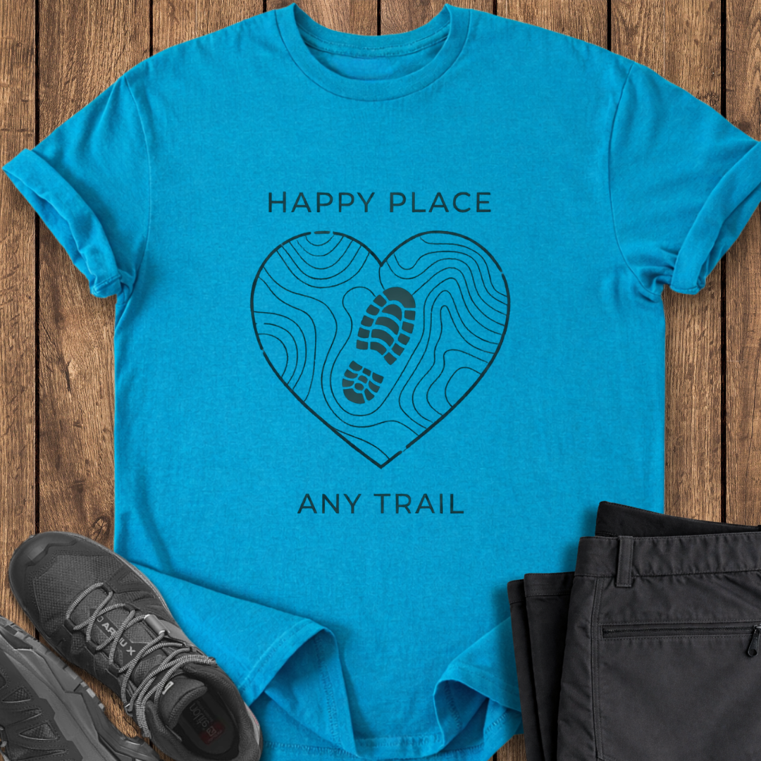 Blue t-shirt with 'Happy Place, Any Trail' design on a wooden surface with shoes and pants. hiking t shirt