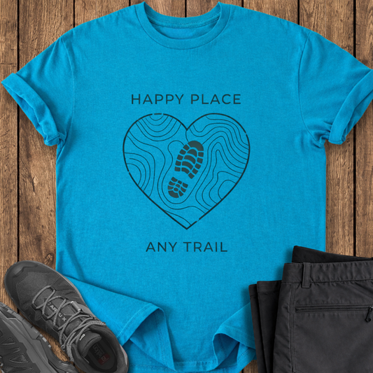 Blue t-shirt with 'Happy Place, Any Trail' design on a wooden surface with shoes and pants. hiking t shirt