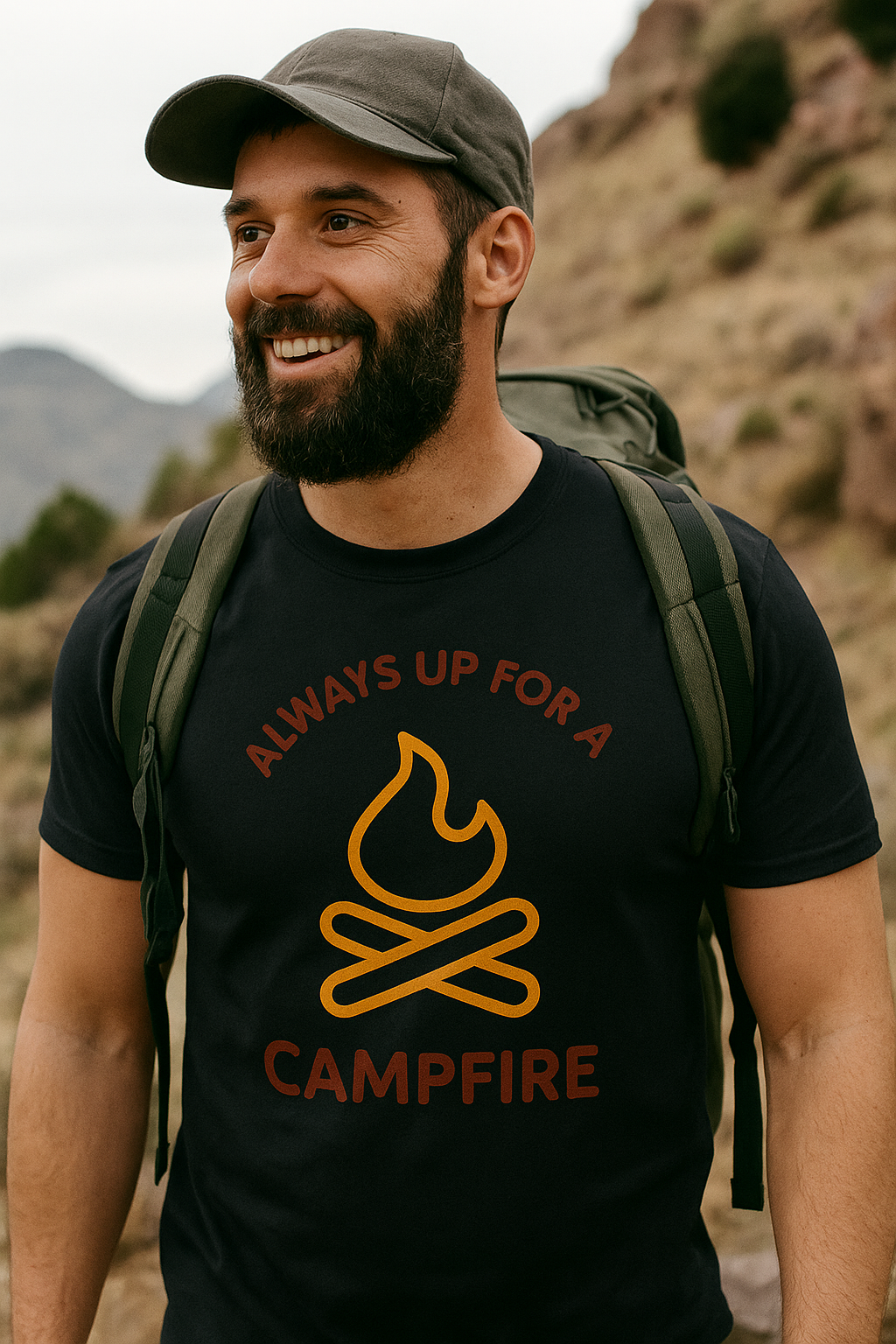 happy hiker wearing a black t-shirt with a campfire graphic and text, standing outdoors with mountains in the background.